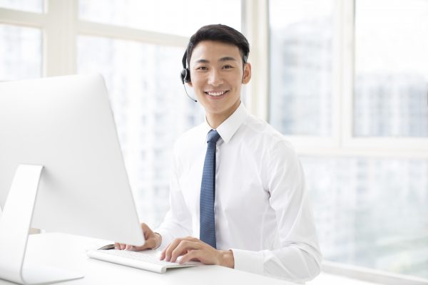 Cheerful young Chinese businessman working in office with headset